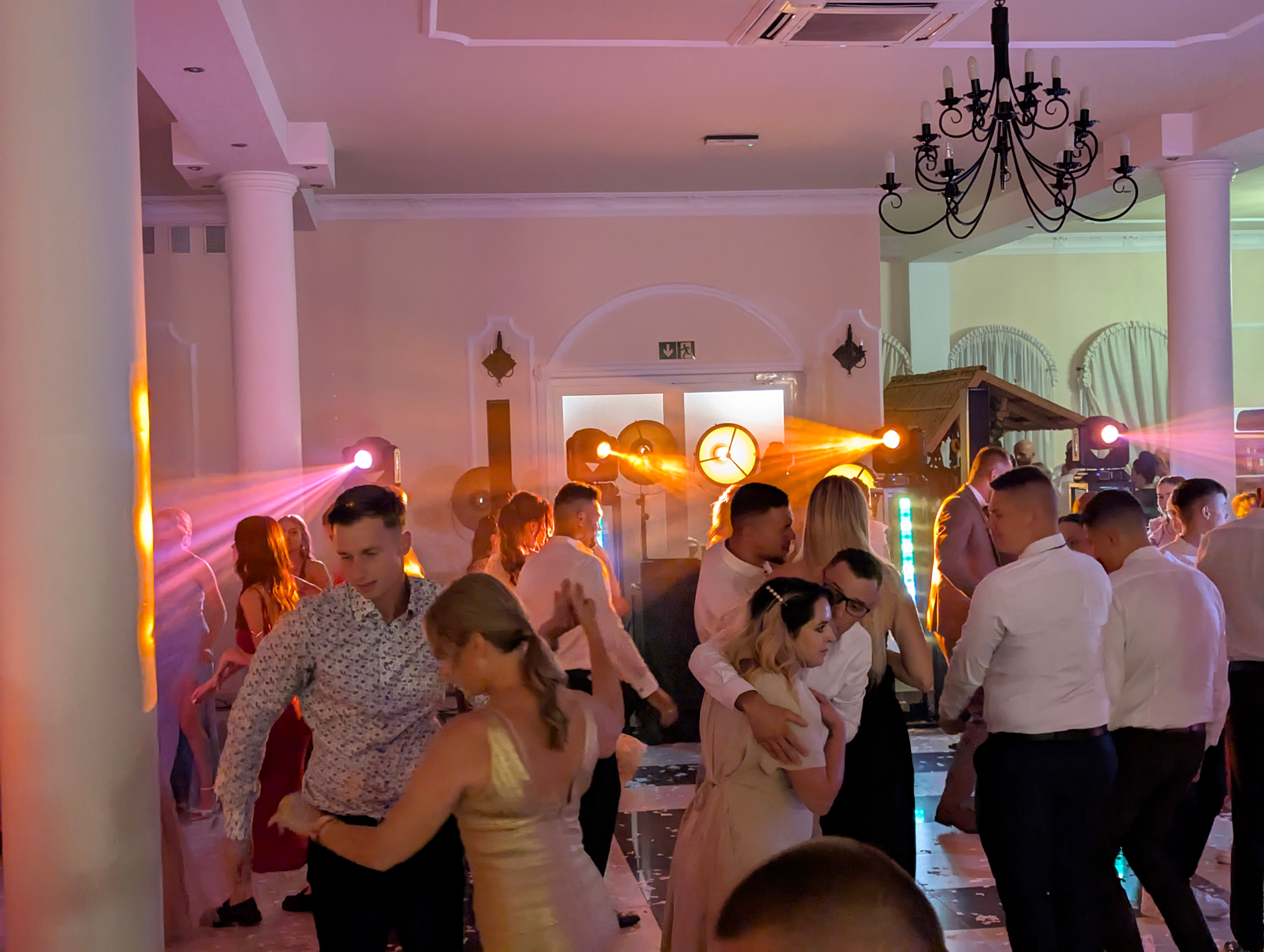 Elegancka sala balowa z tańczącymi gośćmi i różowym oświetleniem atmosferycznym
